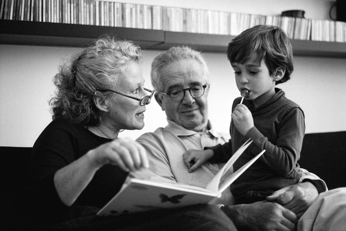 Des grands-parents lisent un livre à leur petit fils qui mange une sucette